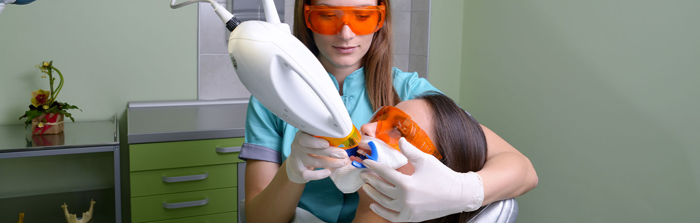 Female dentist providing teeth whitening treatment to the patient