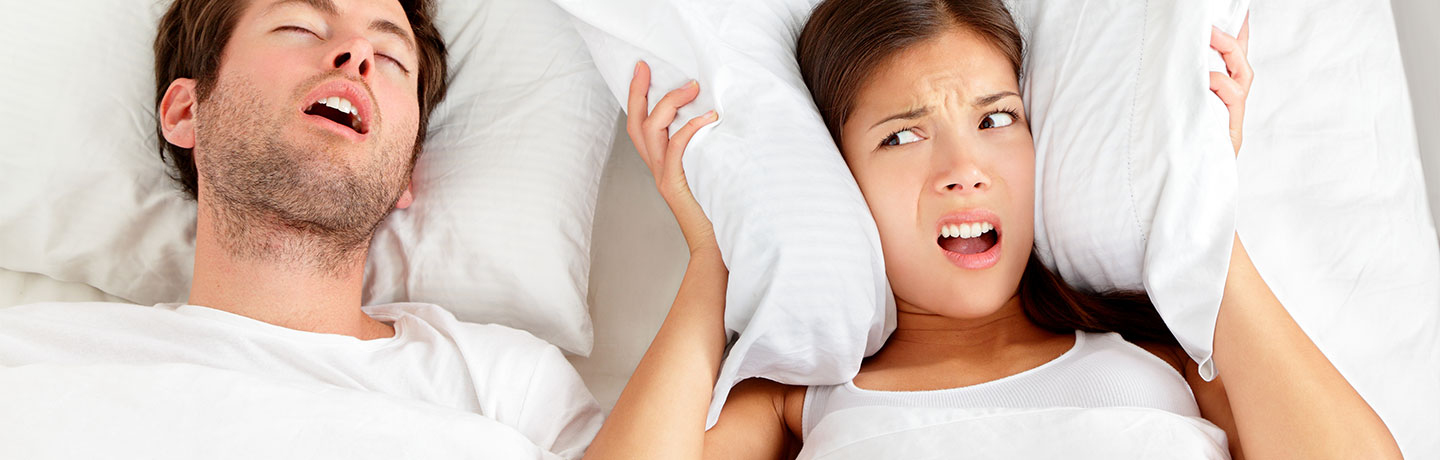 A young female lady closing her ears with pillows to avoid her boyfriend's snoring